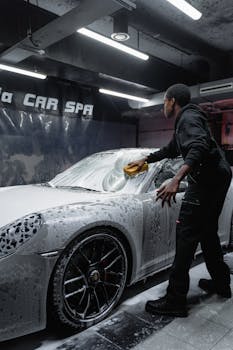 Employee in uniform cleaning a luxury car with foa