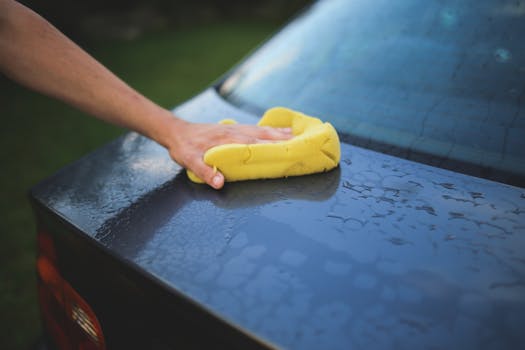 Hand cleaning car with a yellow sponge showcasing