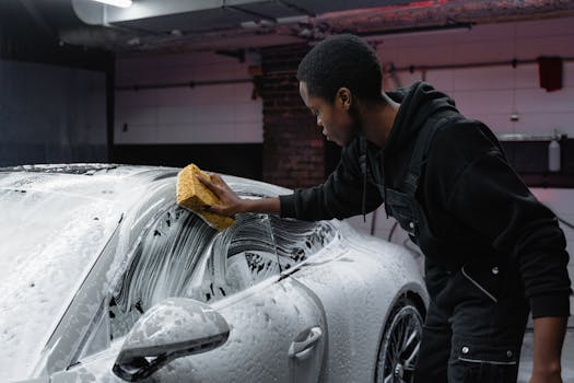 A young man cleans a luxury car with a sponge in a