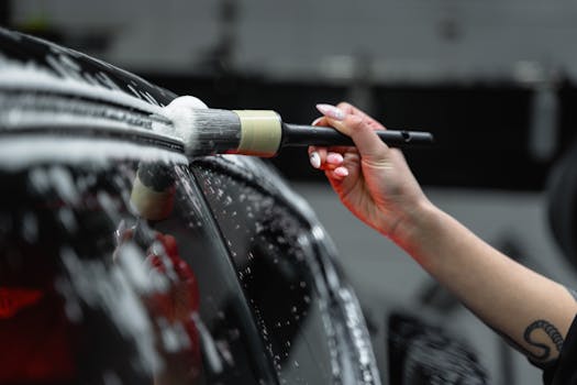 Hand cleaning car exterior with brush and foam in