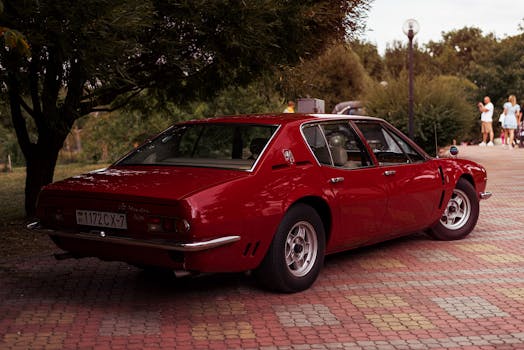 A shiny red vintage car parked under trees in an o