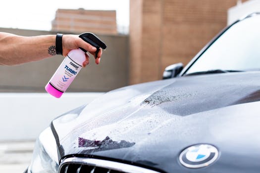 Hand applying cleaning spray on a wet BMW hood for