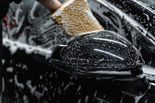 Hand scrubbing a car mirror with a sponge covered